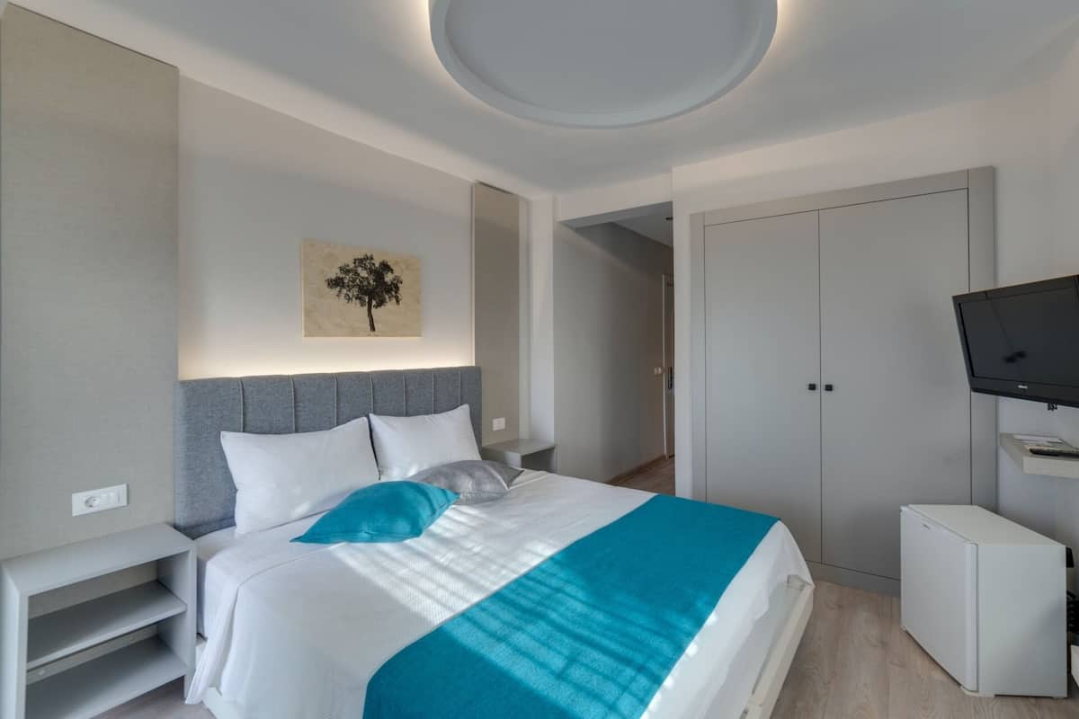 A modern hotel room with a bed, a TV, a wardrobe, and a small desk.