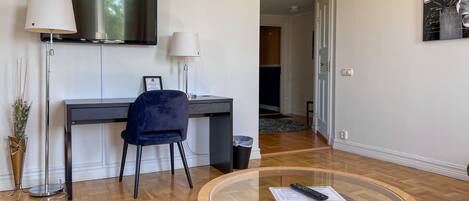 Una sala de estar moderna con una televisión de pantalla plana, un escritorio con una silla, una mesa de centro de vidrio y una gran obra de arte floral en la pared.