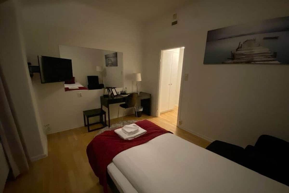 A hotel room with a bed, a desk, a chair, a television, and a door.