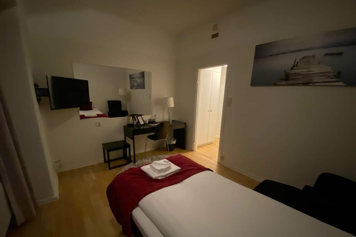 A hotel room with a bed, a desk, a chair, a TV, and a door leading to another room.