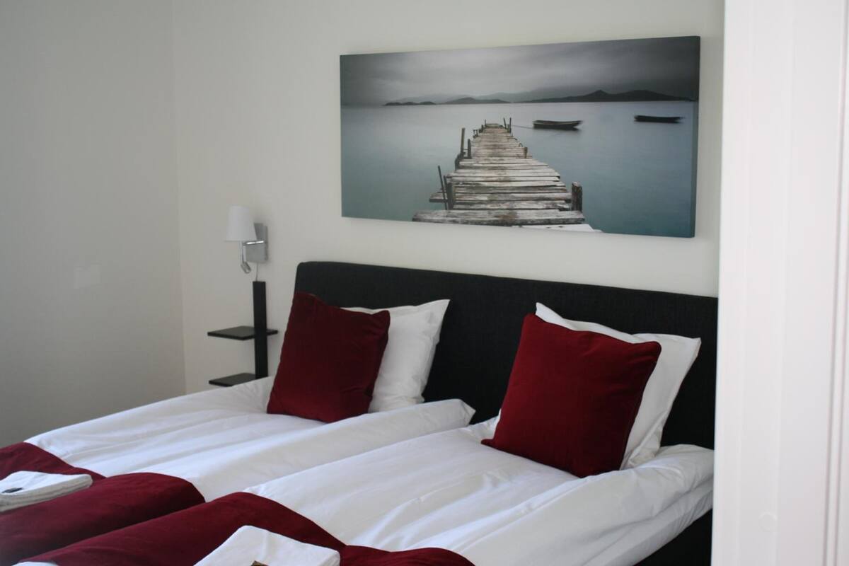A hotel room with a bed, a nightstand, a lamp, and a painting of a pier.