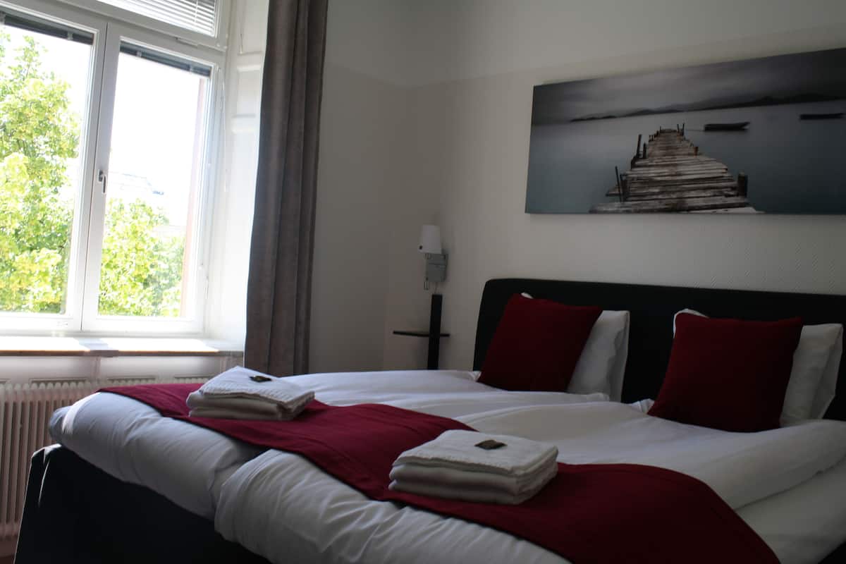 A hotel room with a large bed, a view of the outdoors through a window, and a painting on the wall.