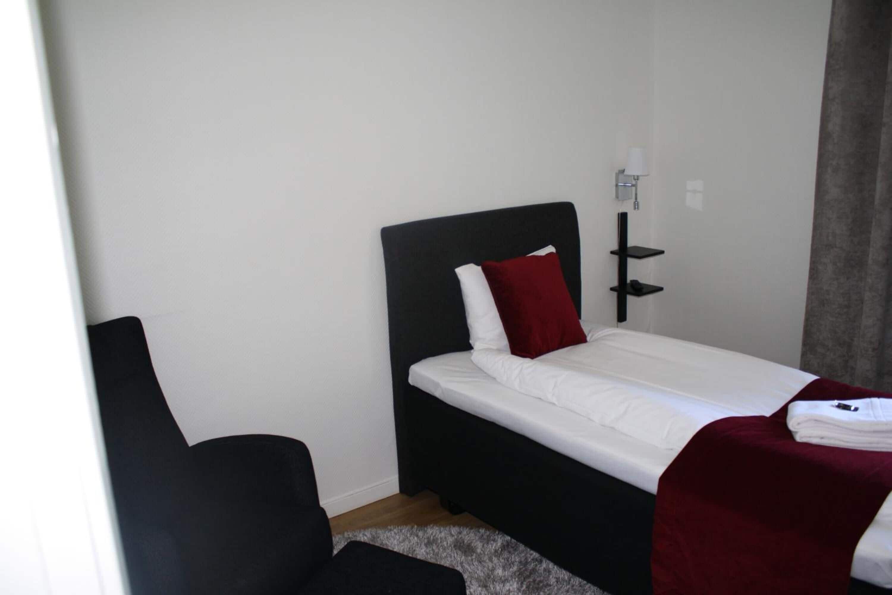 A small, neatly arranged bedroom with a single bed, a chair, and a bedside table.