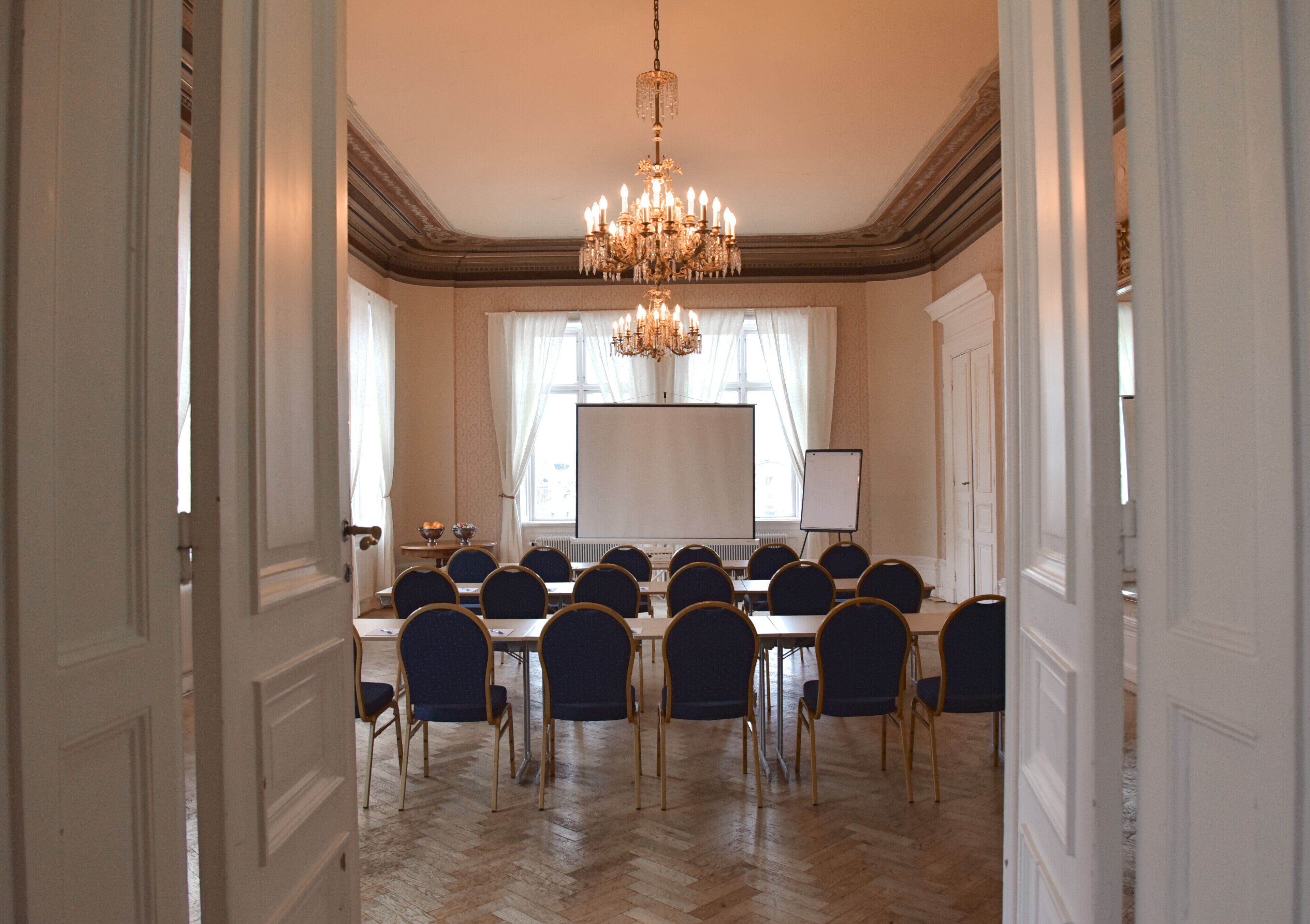 A conference room with a large table, chairs, a projector screen, and a chandelier.