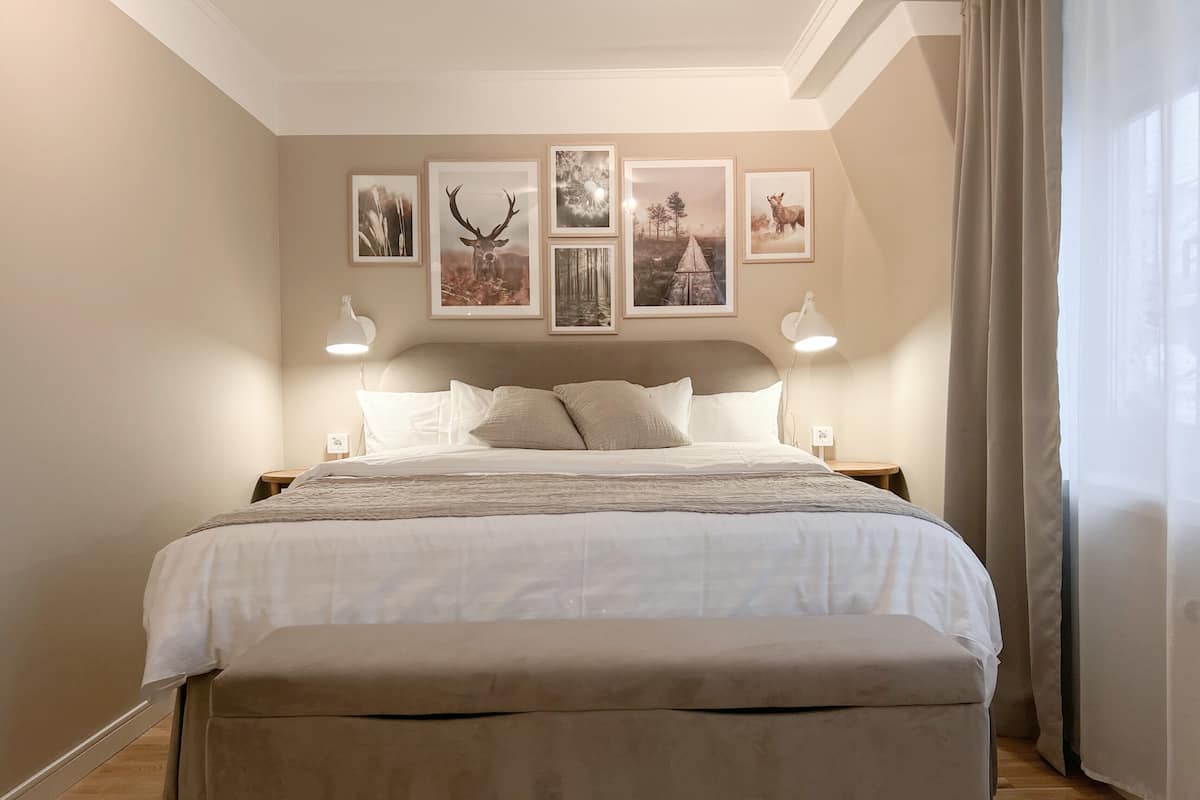 A neatly arranged bedroom with a large bed, two bedside lamps, and a series of framed pictures on the wall.