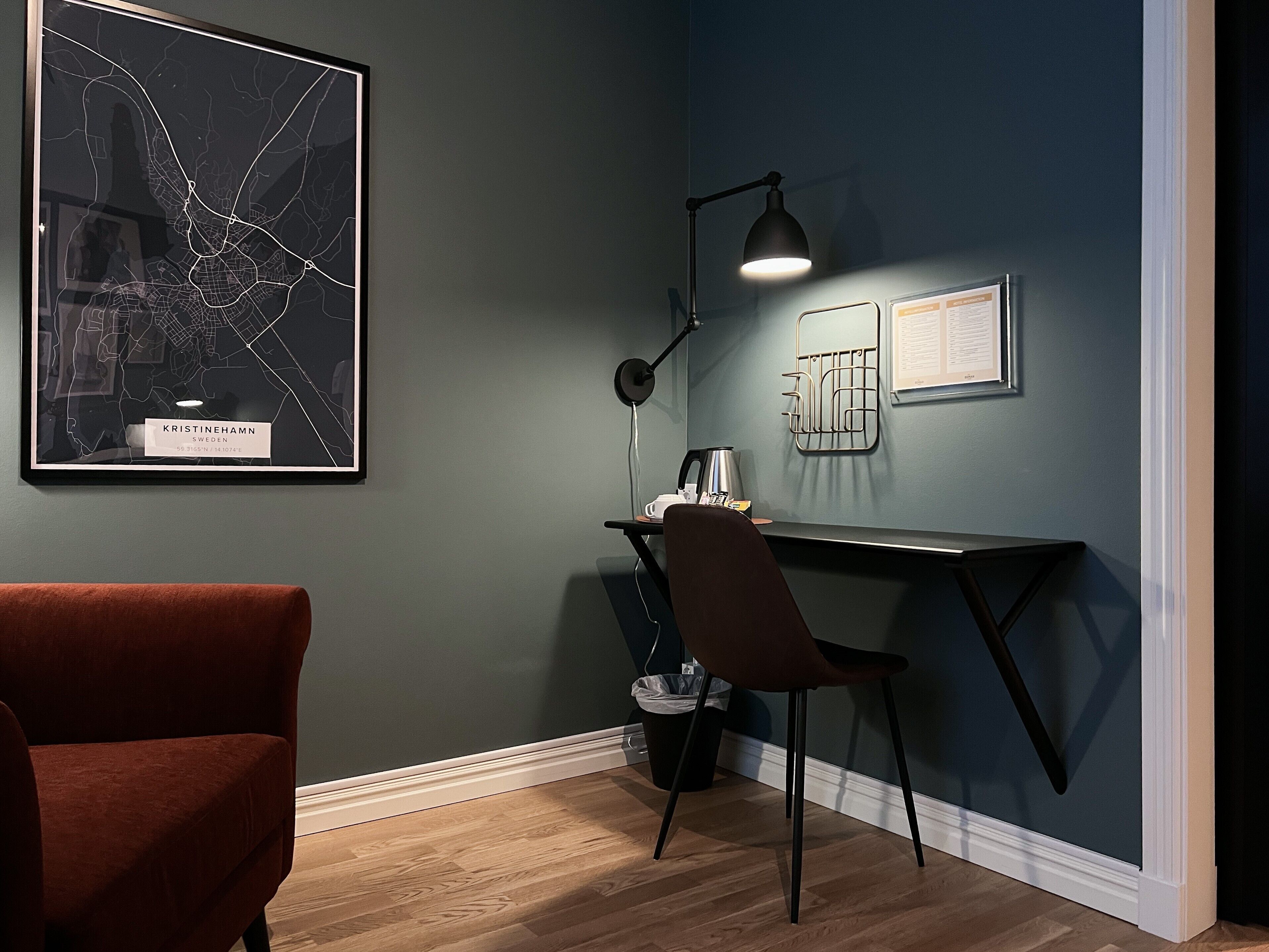 A room with a dark blue wall, a framed map, a desk with a chair, a lamp, and a red chair.
