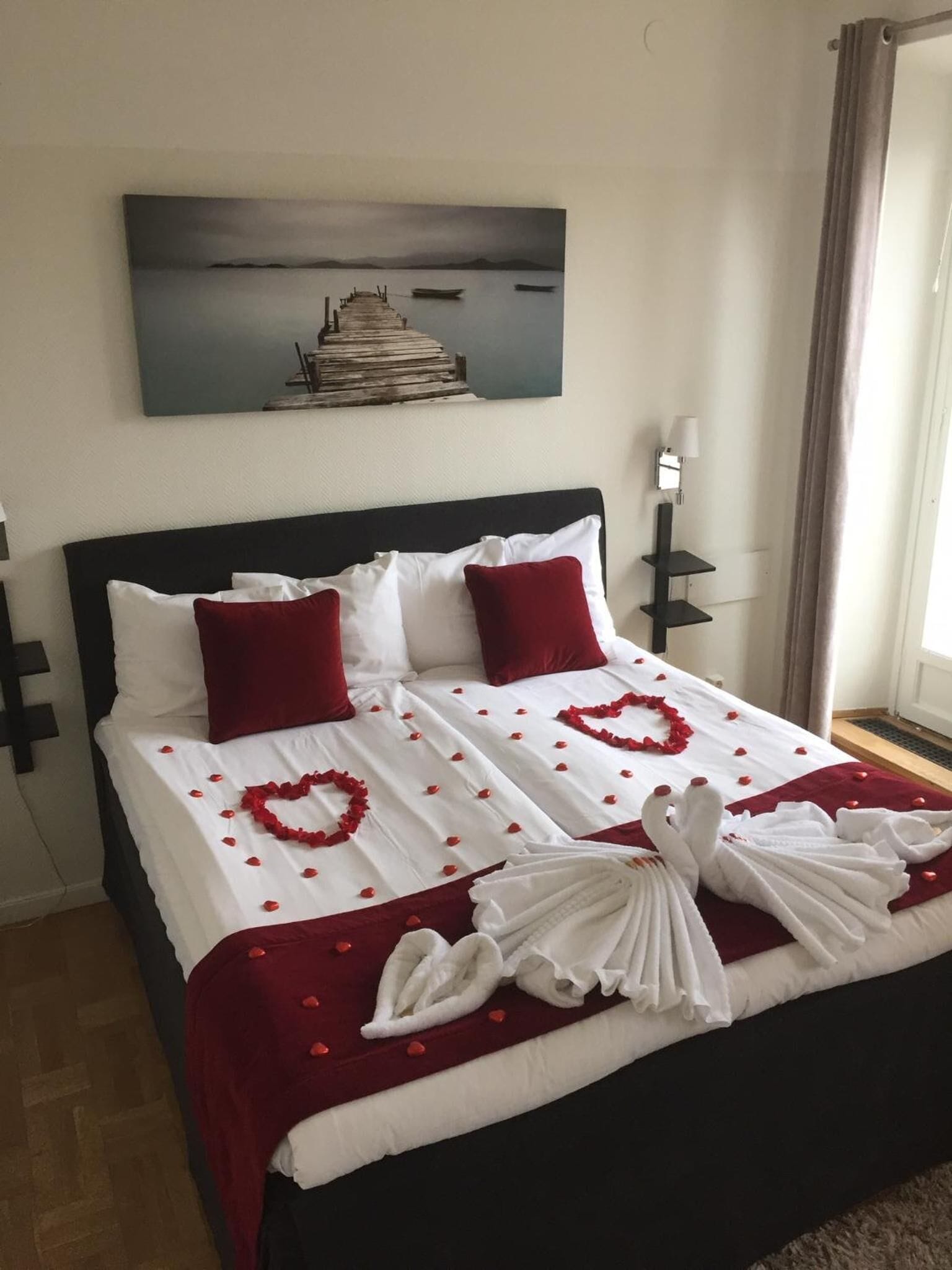 A neatly made bed with red and white linens, a heart-shaped decoration, and a towel arrangement.