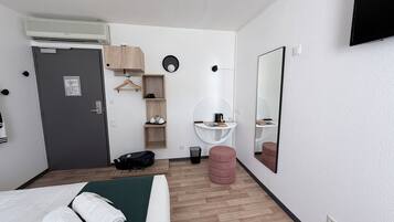 Et hotelværelse med seng, skrivebord, spejl, garderobe og et lille badeværelse.