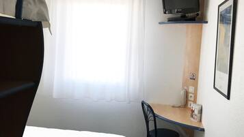 Habitación de hotel con literas, un escritorio con silla, un televisor montado en la pared y una ventana con cortinas.