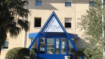 A hotel entrance with a blue awning, a clear sky, and a pathway leading to the door.