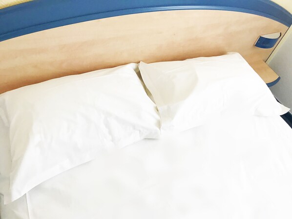 Una cama con sábanas y almohadas blancas, un cabecero de madera y un objeto azul pequeño al lado.