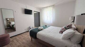 A hotel room with a bed, a mirror, a TV, a window with curtains, and a bedside table.