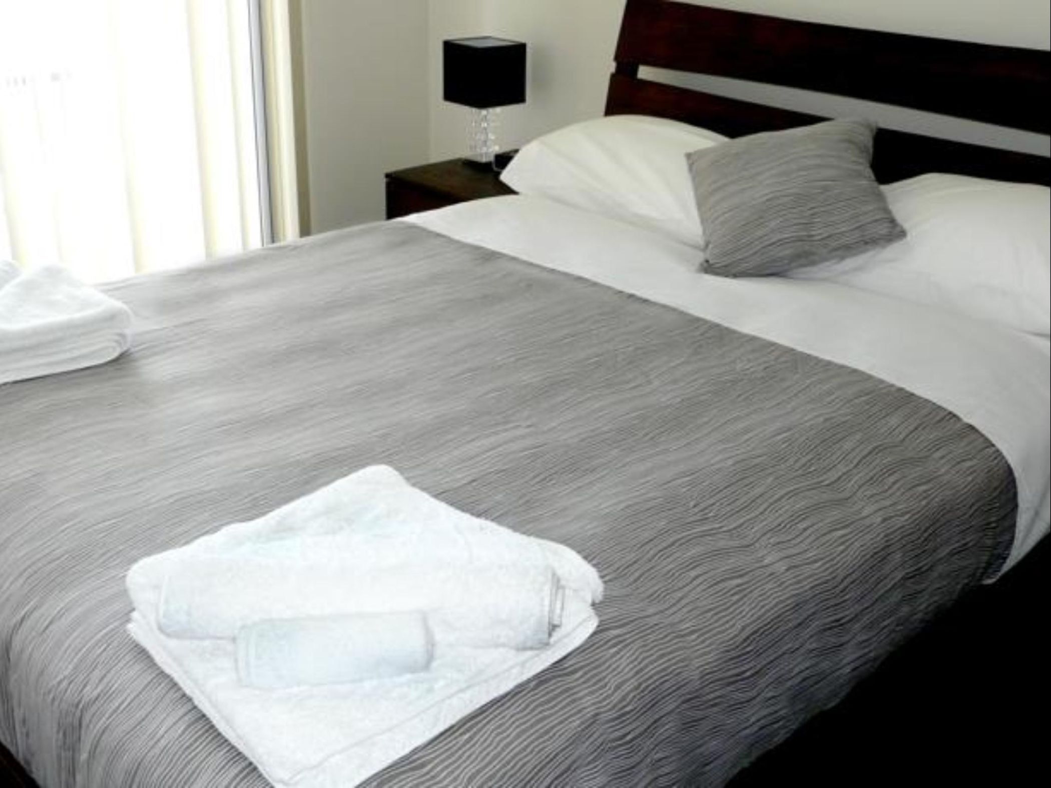 A neatly made bed with a grey and white patterned bedspread, a grey pillow, and a white towel on the side.