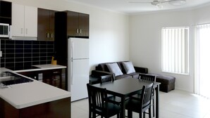 A modern kitchen with dark cabinets, a white refrigerator, and a dining area with a table and chairs. - Monterey Moranbah (Moranbah)