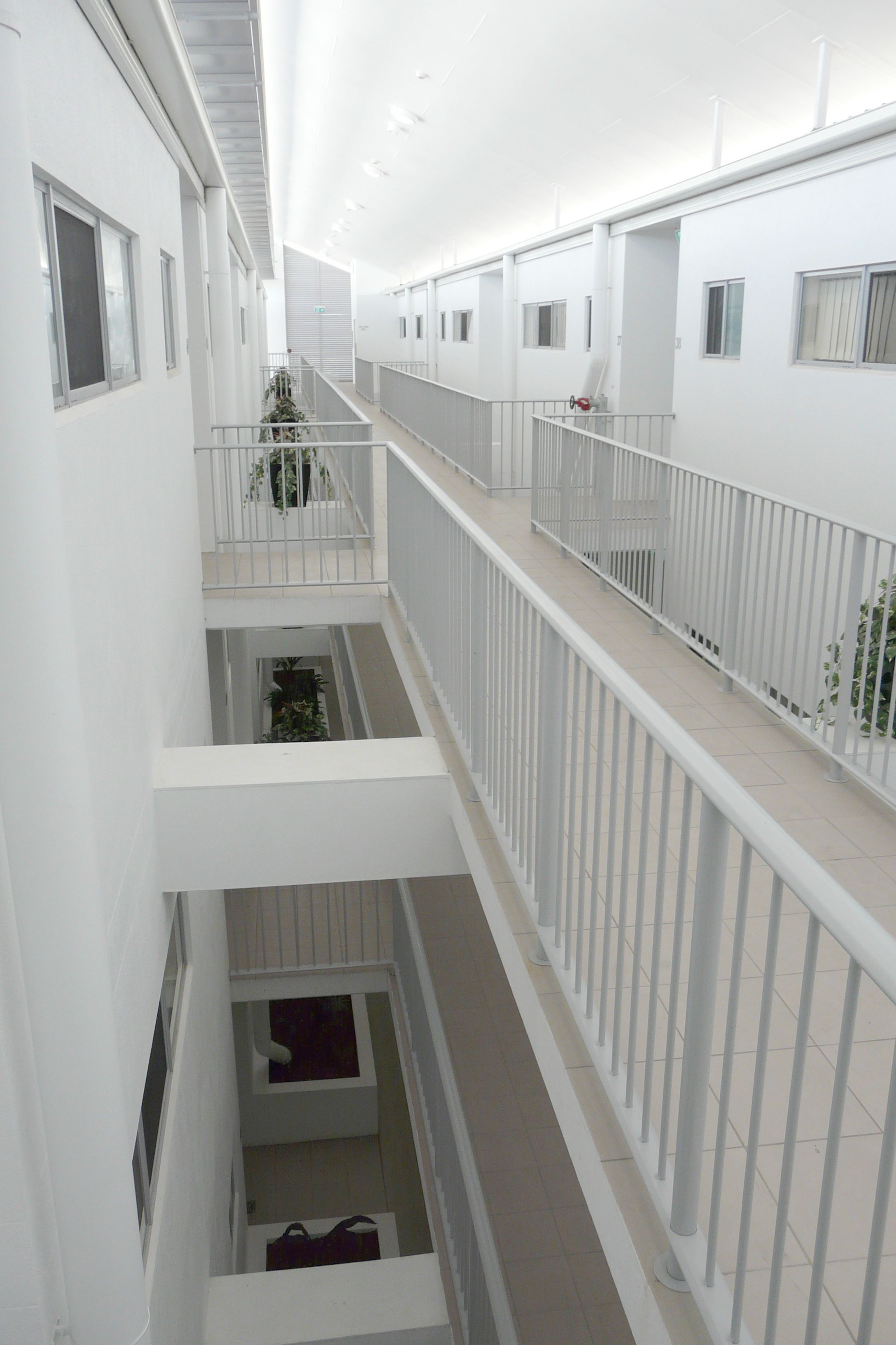 A multi-level interior with white walls and railings, featuring balconies with potted plants and a staircase connecting the levels.