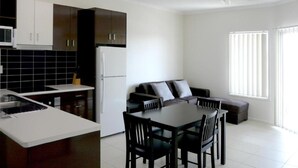 A modern kitchen with dark cabinets, a white refrigerator, and a dining area with a table and chairs. - Monterey Moranbah (Moranbah)