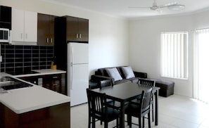 A modern kitchen with dark cabinets, a white refrigerator, and a dining area with a table and chairs. - Monterey Moranbah (Moranbah)