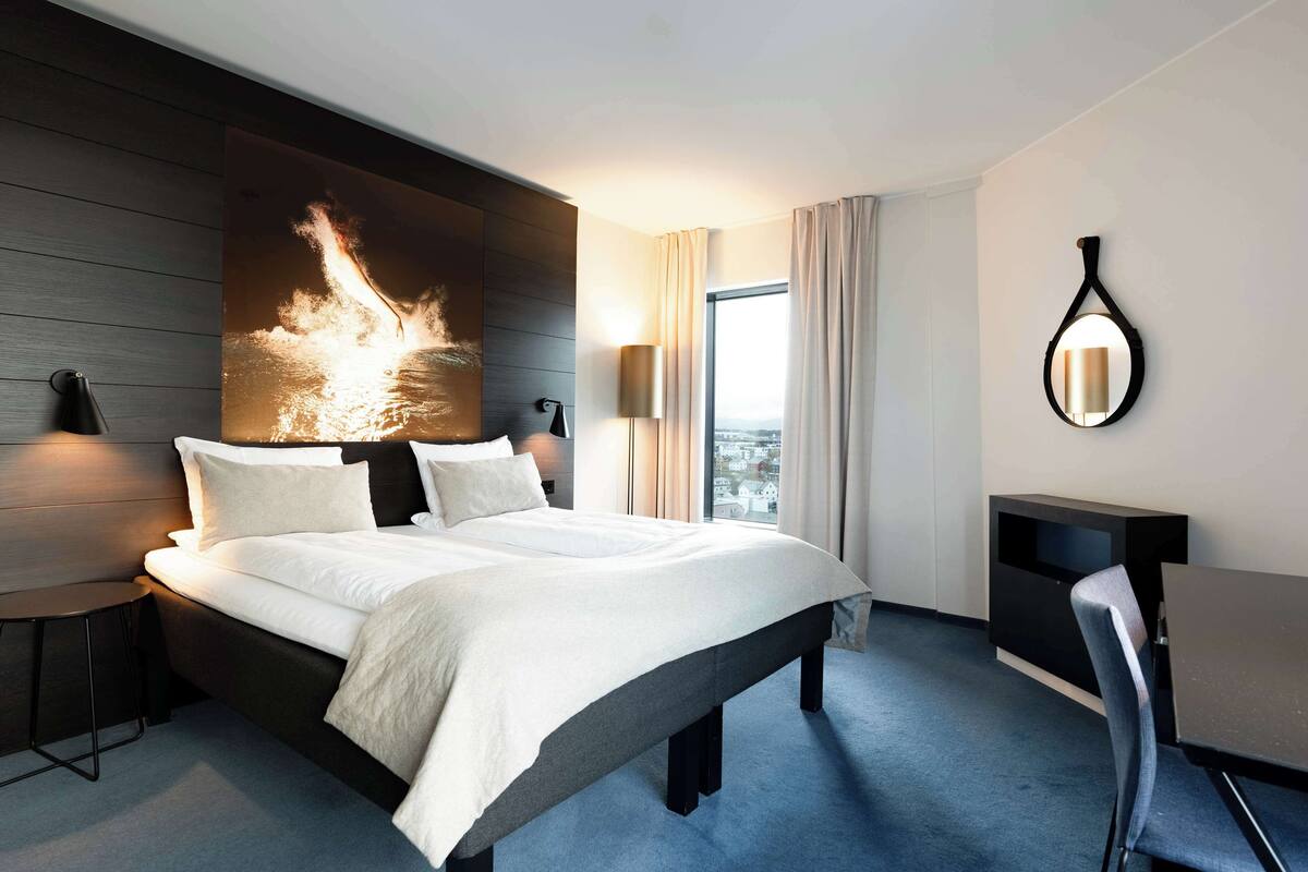 A modern hotel room with a large bed, a desk, and a view of the city.