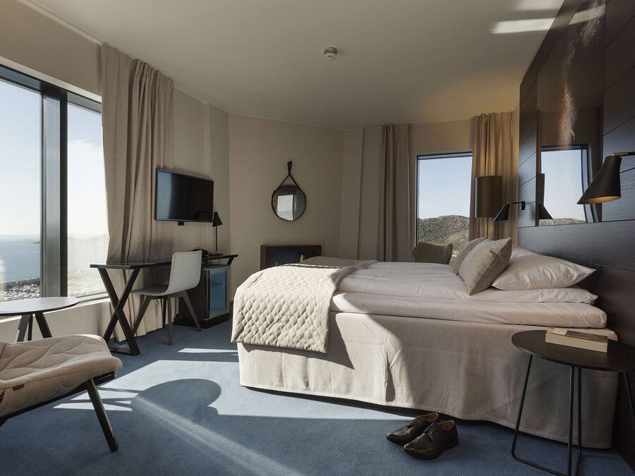 Una habitación de hotel moderna con una cama grande, un escritorio, una silla y un televisor.