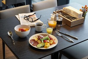 A breakfast table with a newspaper, a bowl of cereal, a cup of coffee, a glass of orange juice, and a plate of eggs, bacon, and vegetables.