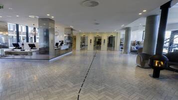 A spacious lobby with a herringbone floor pattern, a reception desk with computers, and a seating area with a modern fireplace.