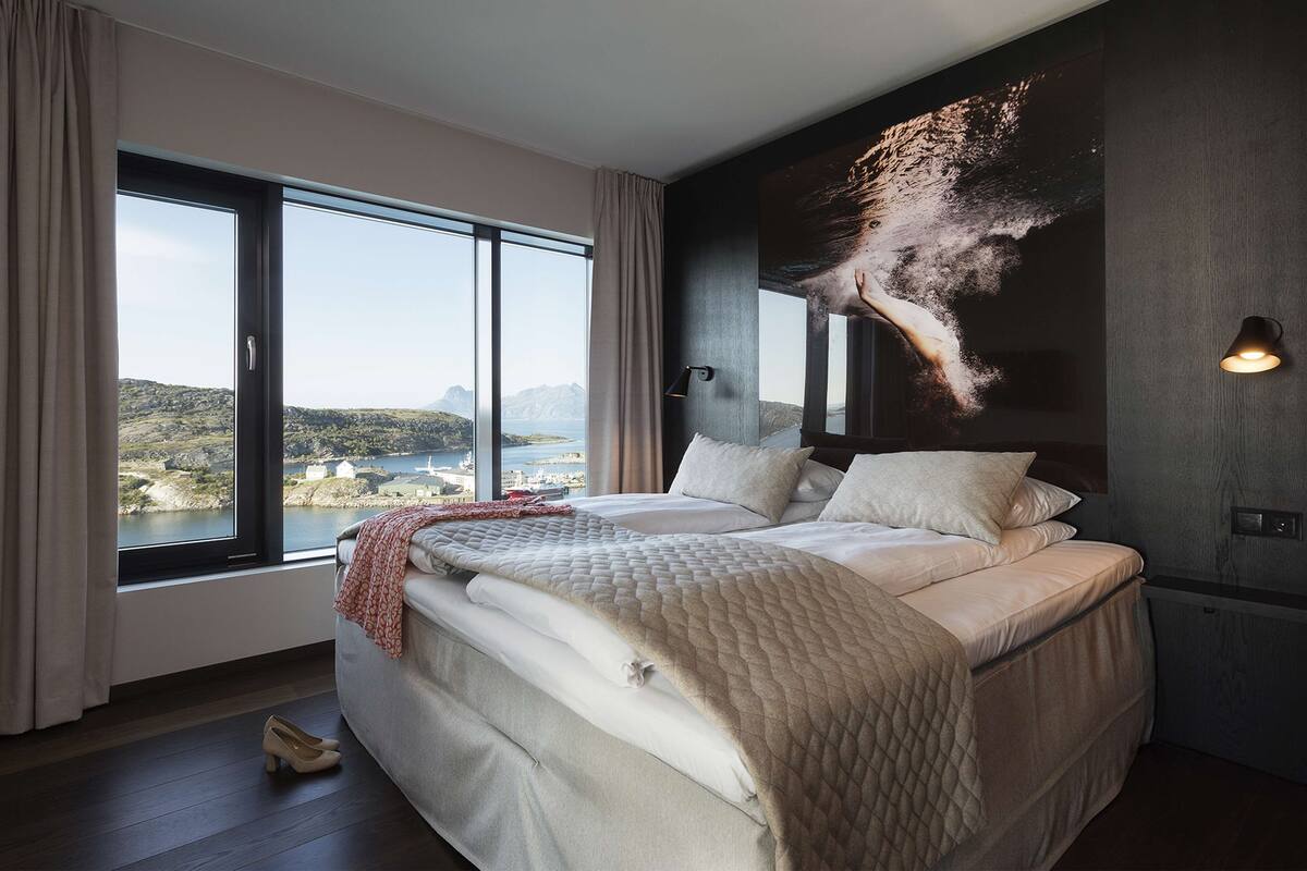 A bedroom with a large bed, a view of the sea, and a wall-mounted light fixture.