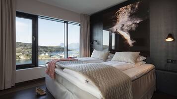 A bedroom with a large bed, a view of the sea, and a wall-mounted light fixture.