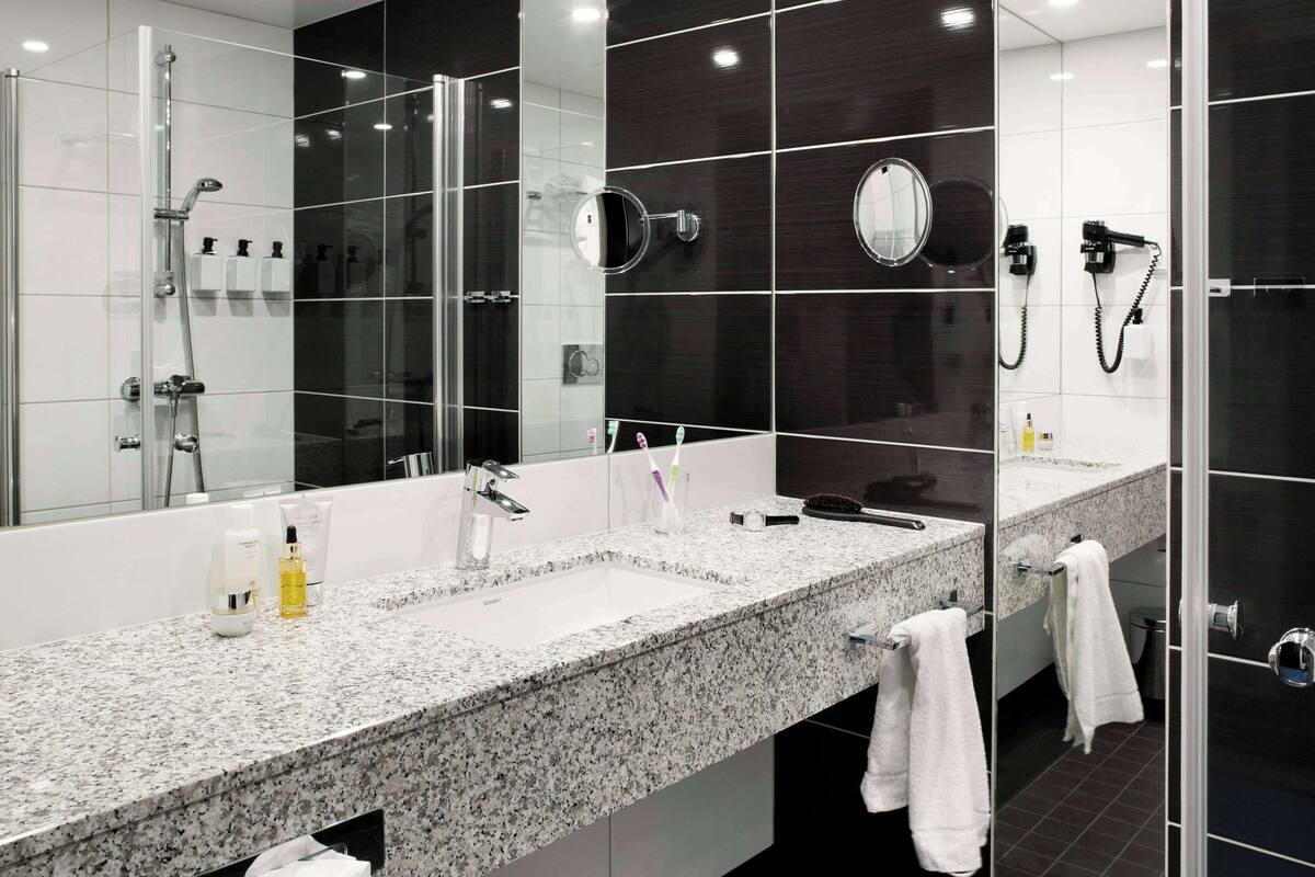 Un baño moderno con un espejo grande, dos lavamanos, ducha y secador de pelo.