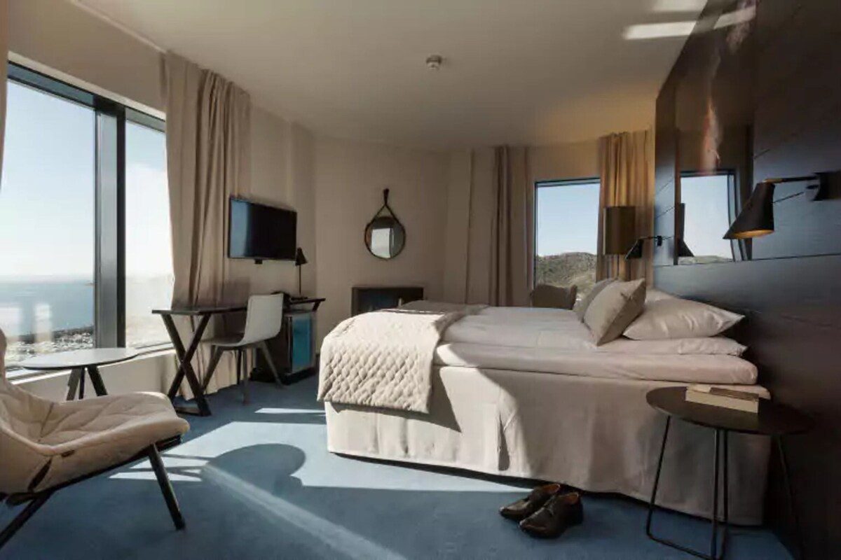 A modern hotel room with a large bed, a desk, a chair, and a TV.