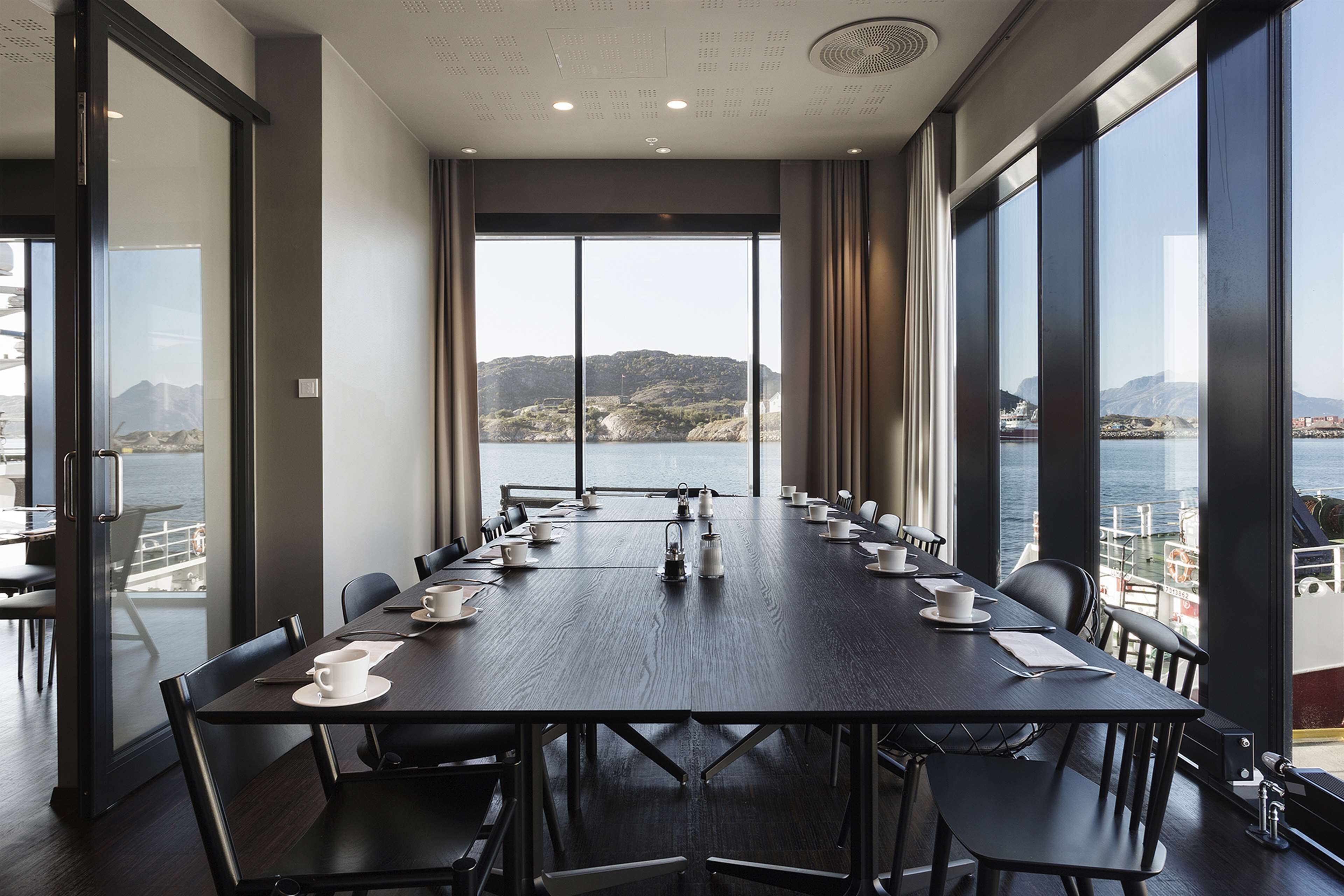Een vergaderzaal met een lange tafel, stoelen en uitzicht op een waterpartij en heuvels.