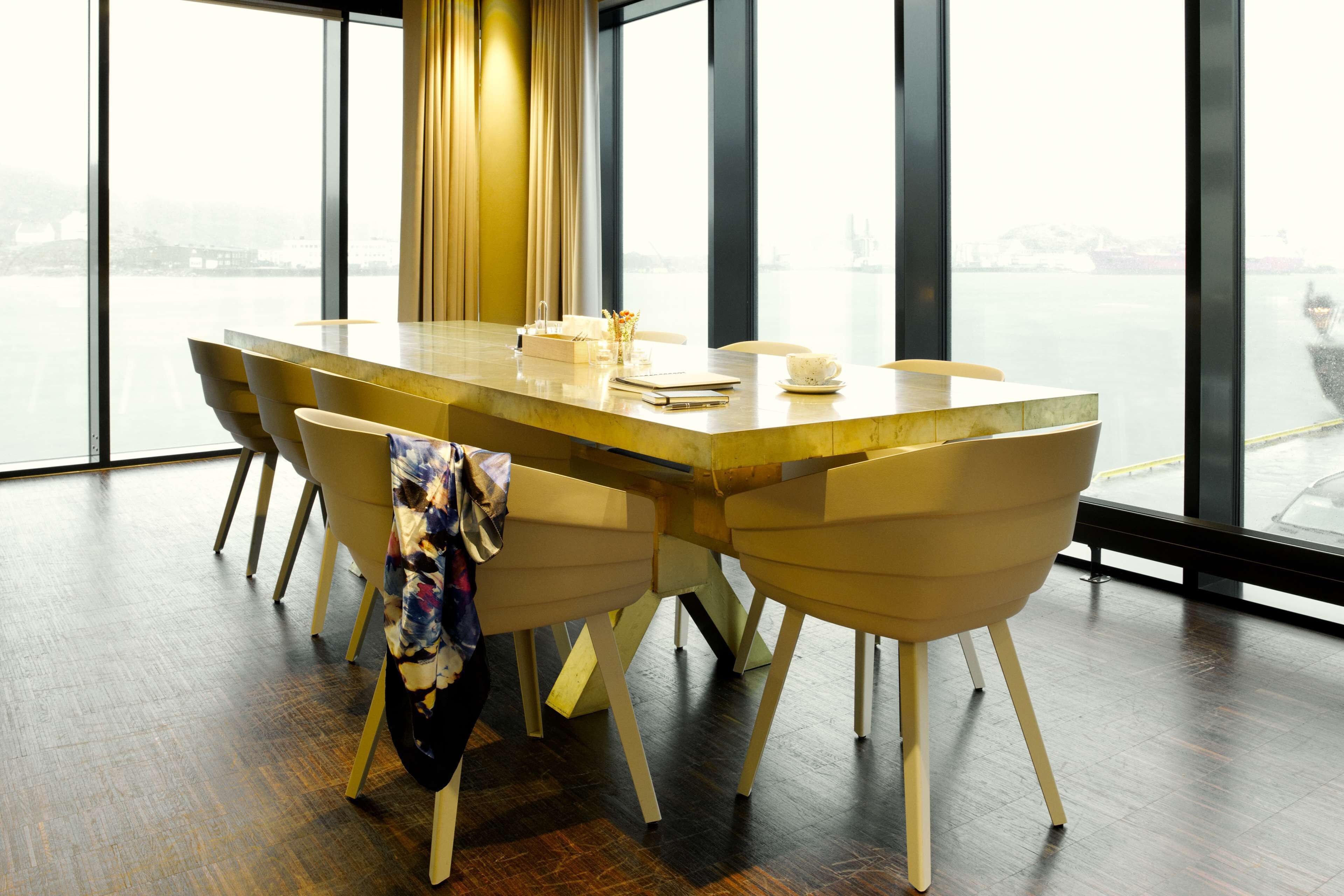 Comedor moderno con una mesa grande, sillas y vistas a una masa de agua a través de amplios ventanales.