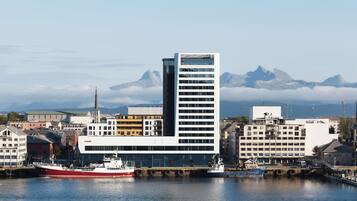 A modern building with a prominent tower, situated by a calm harbor with boats.
