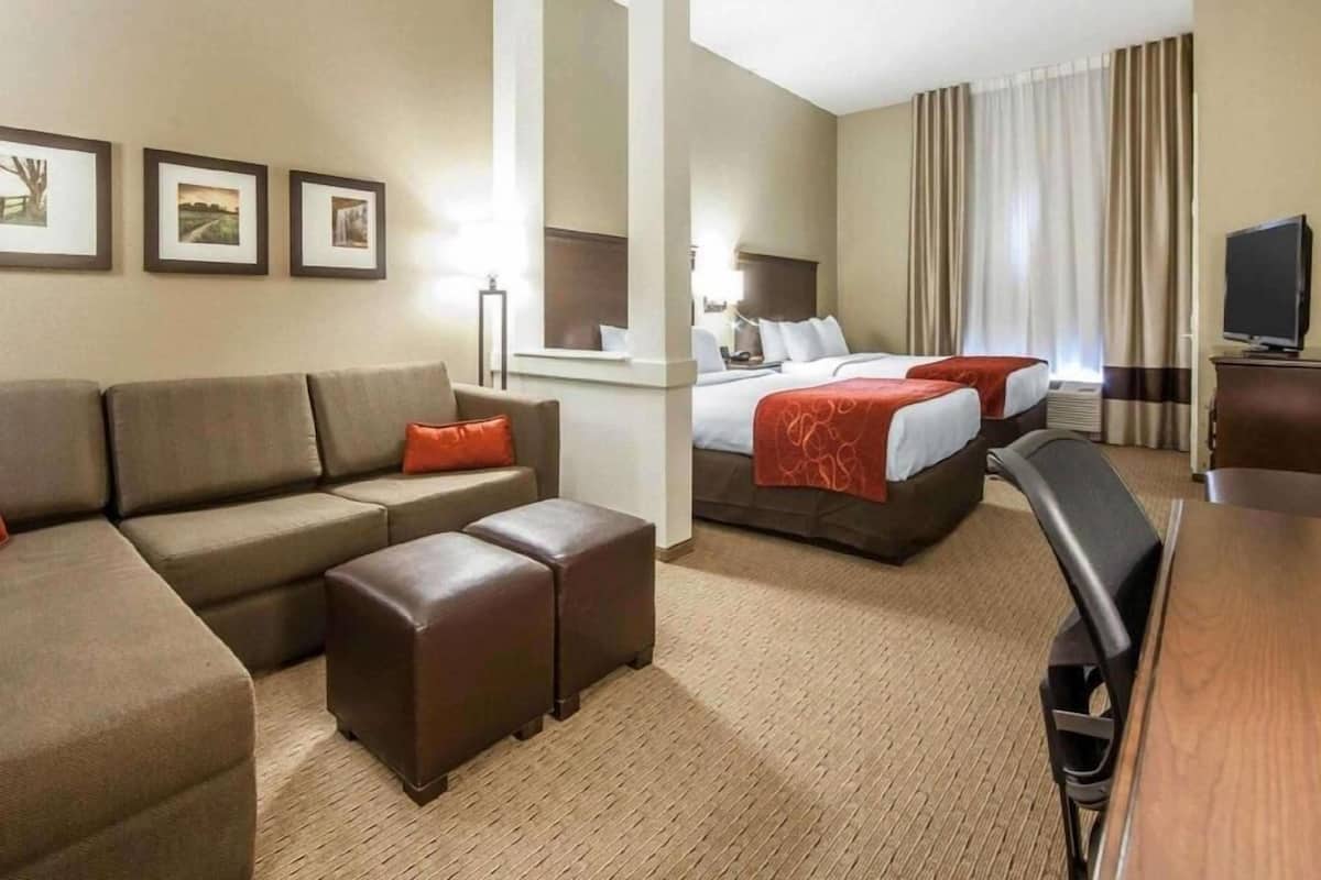 A hotel room with a sofa, two beds, a TV, and framed pictures on the wall.