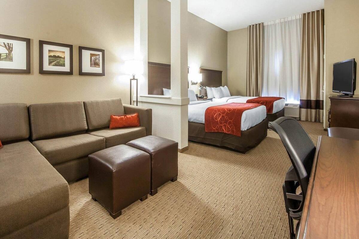 A hotel room with a sofa, two beds, a TV, and framed pictures on the wall.