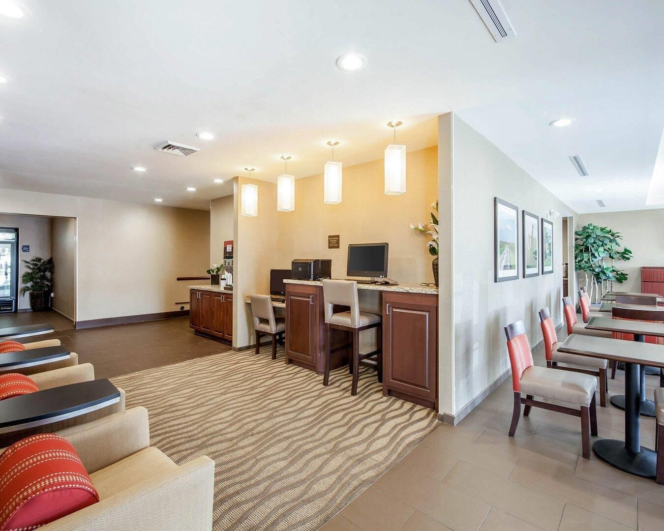 A hotel lobby with a reception desk, computers, seating area, and a dining section.