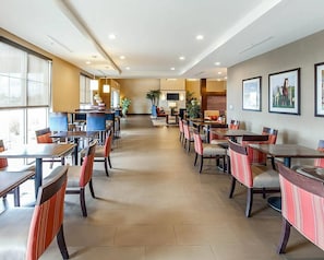 A hotel lobby with multiple dining tables and chairs, a reception desk, and framed pictures on the walls. - Comfort Suites Marietta - Parkersburg (Marietta)
