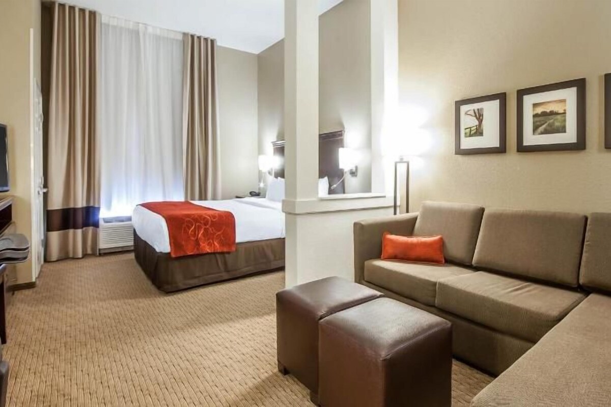 Ein Hotelzimmer mit einem Bett, einem Sofa, einem Hocker, einem Fernseher und gerahmten Bildern an der Wand.