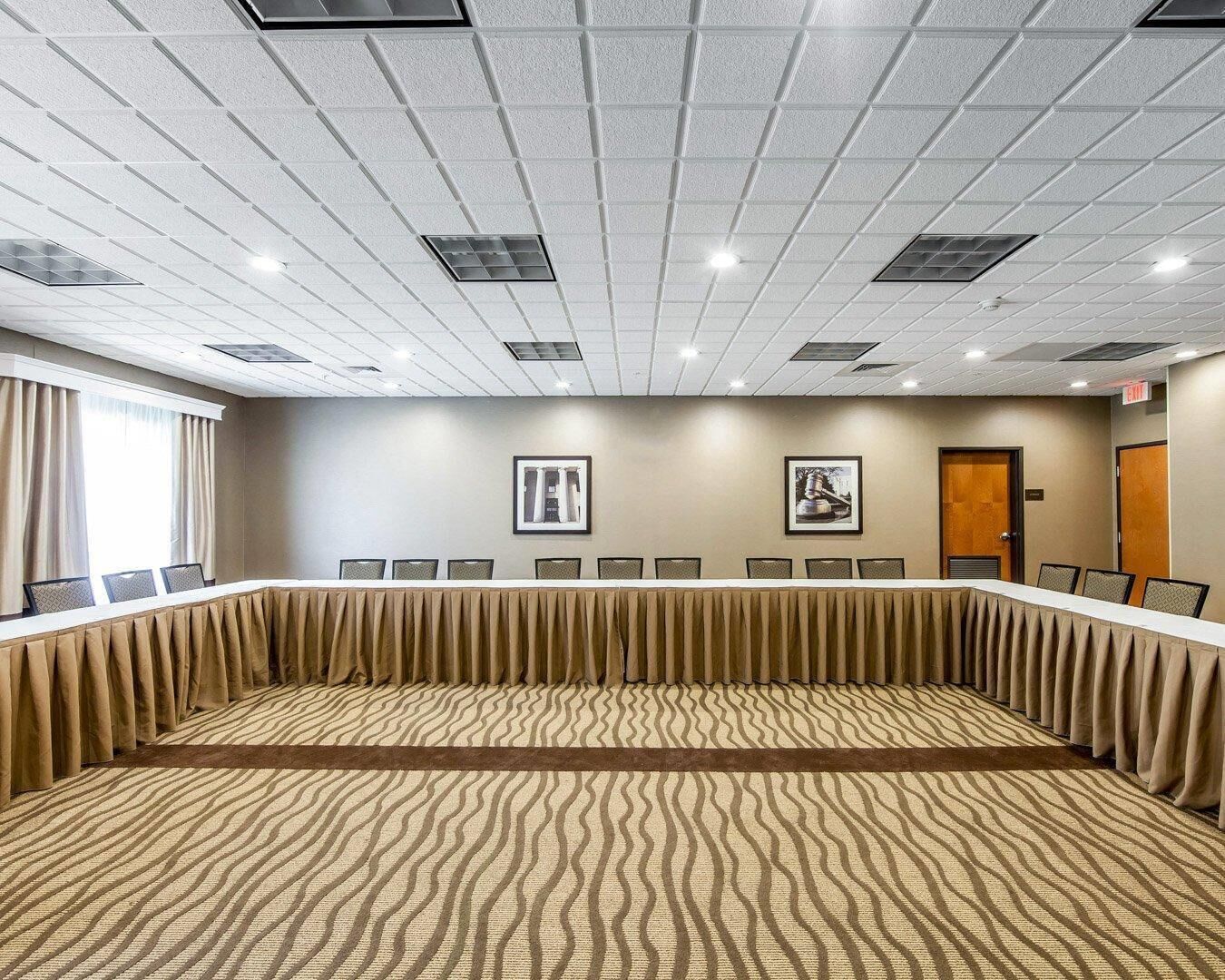 Un salón de conferencias con una larga mesa, sillas, luces de techo y dos cuadros en la pared.