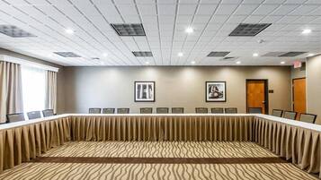 Un salón de conferencias con una larga mesa, sillas, luces de techo y dos cuadros en la pared.