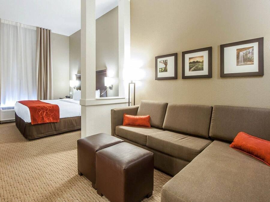 Quarto de hotel com uma cama, um sofá, um banquinho e três quadros na parede.