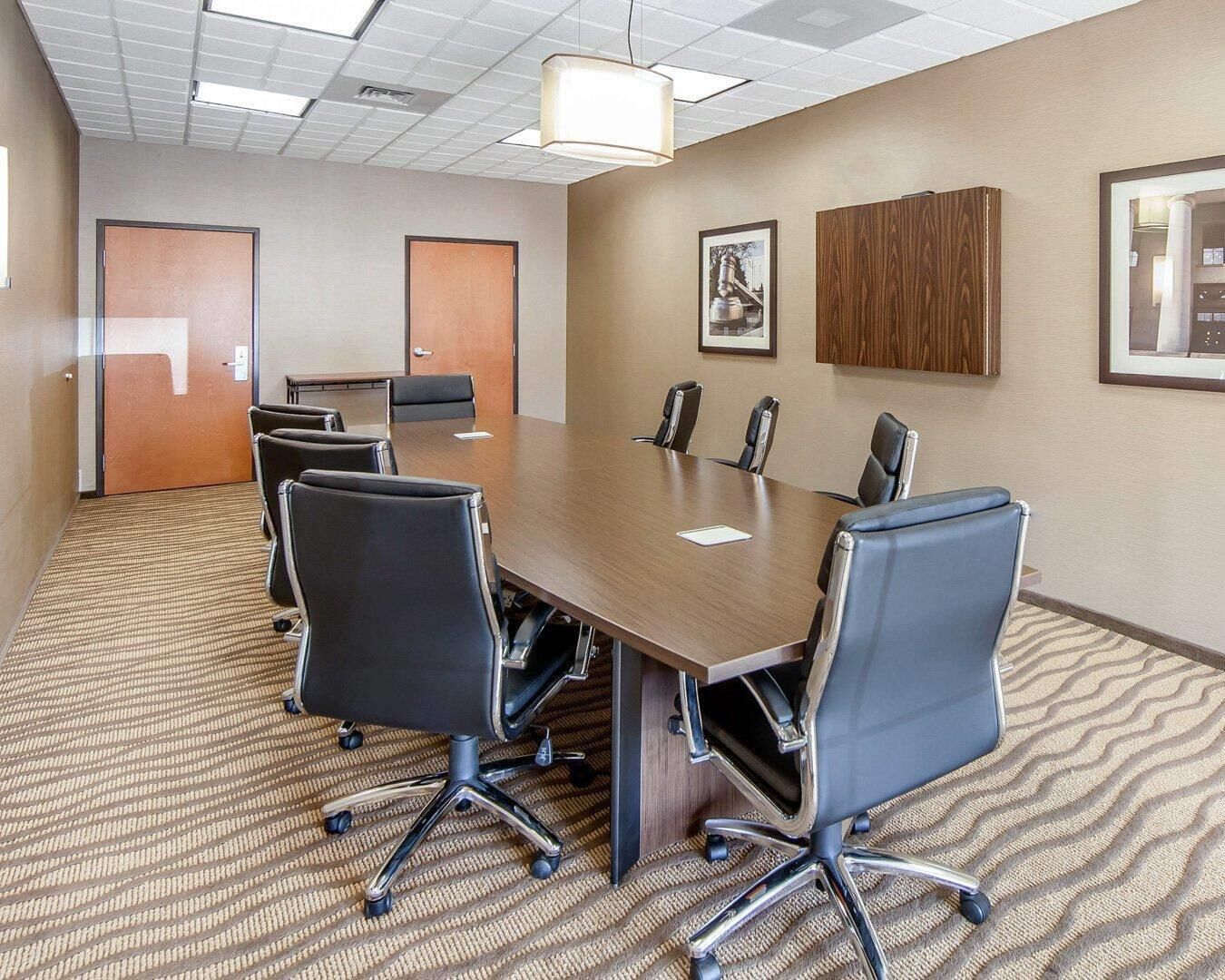A conference room with a long table, six chairs, a wooden cabinet, and framed pictures on the walls.