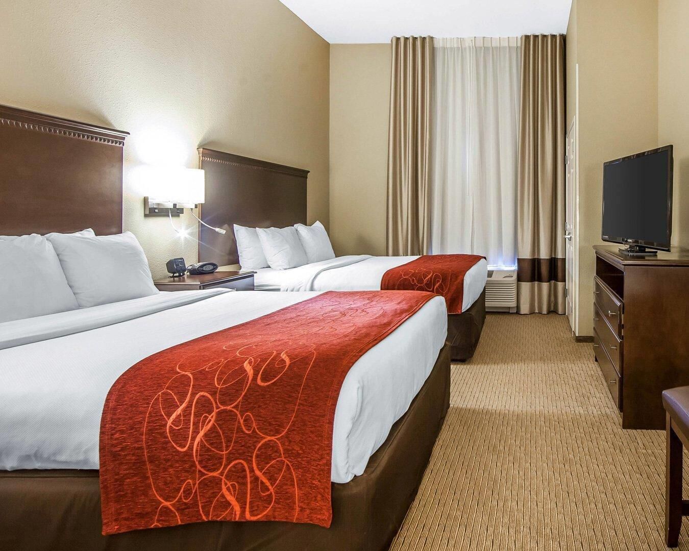 A hotel room with two beds, a TV, a desk, and a chair.