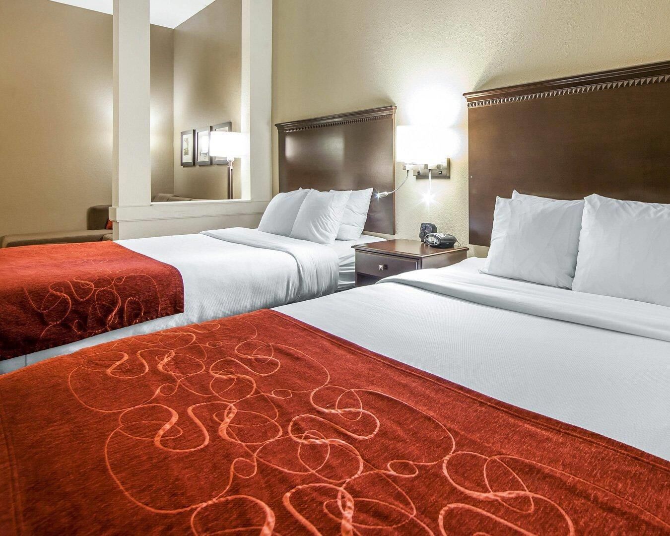 A hotel room with two beds, a nightstand, a lamp, and a mirror.