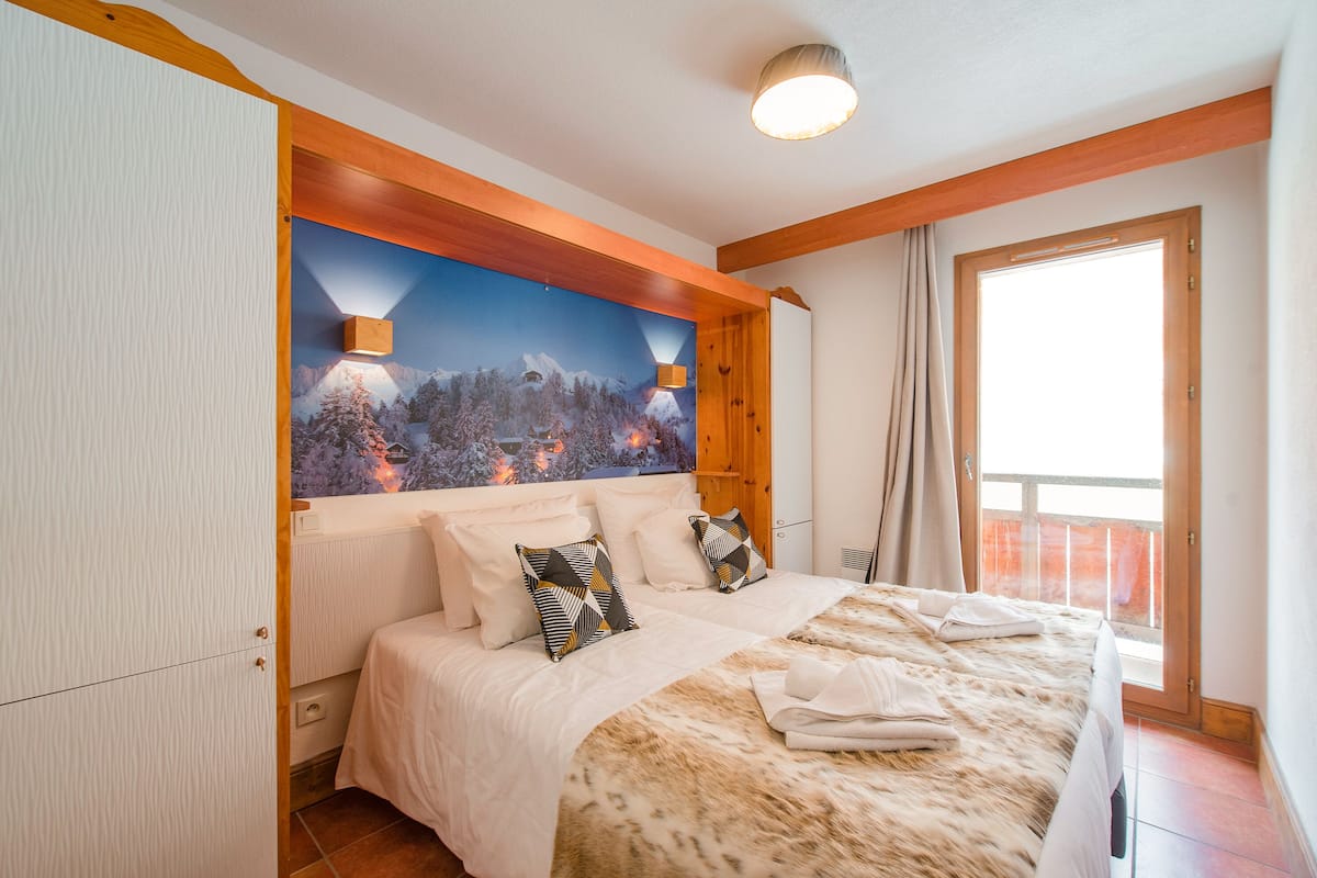 Une chambre avec un grand lit, une fresque murale sur le thème de la montagne, un plafond en bois et une fenêtre avec des rideaux.