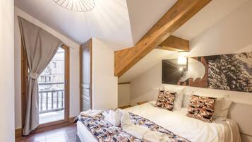 A bedroom with a large bed, wooden beams, a window with curtains, and a wall-mounted light fixture.