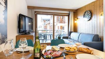Un comedor con una mesa lista para dos personas, con una botella de vino, una tabla de quesos y una variedad de carnes.