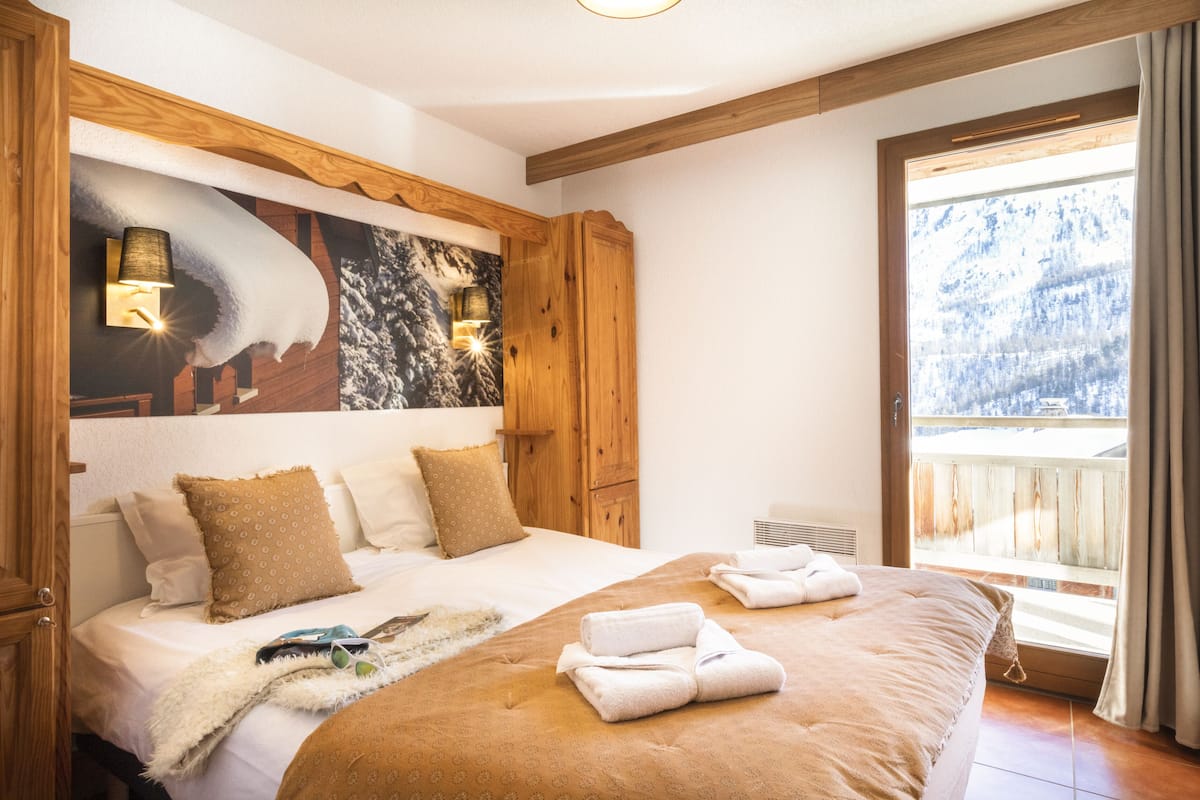 Une chambre avec un grand lit, une tête de lit en bois et une vue sur la montagne par la fenêtre.