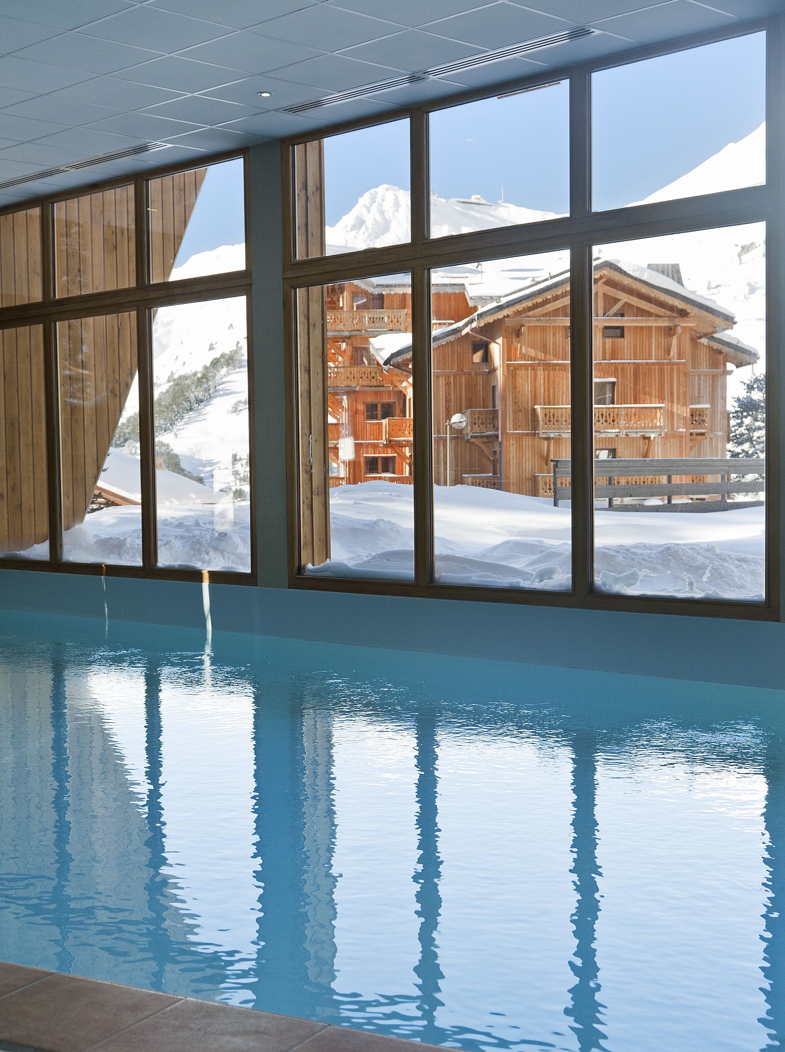 A pool with a view of a wooden building and snowy mountains.