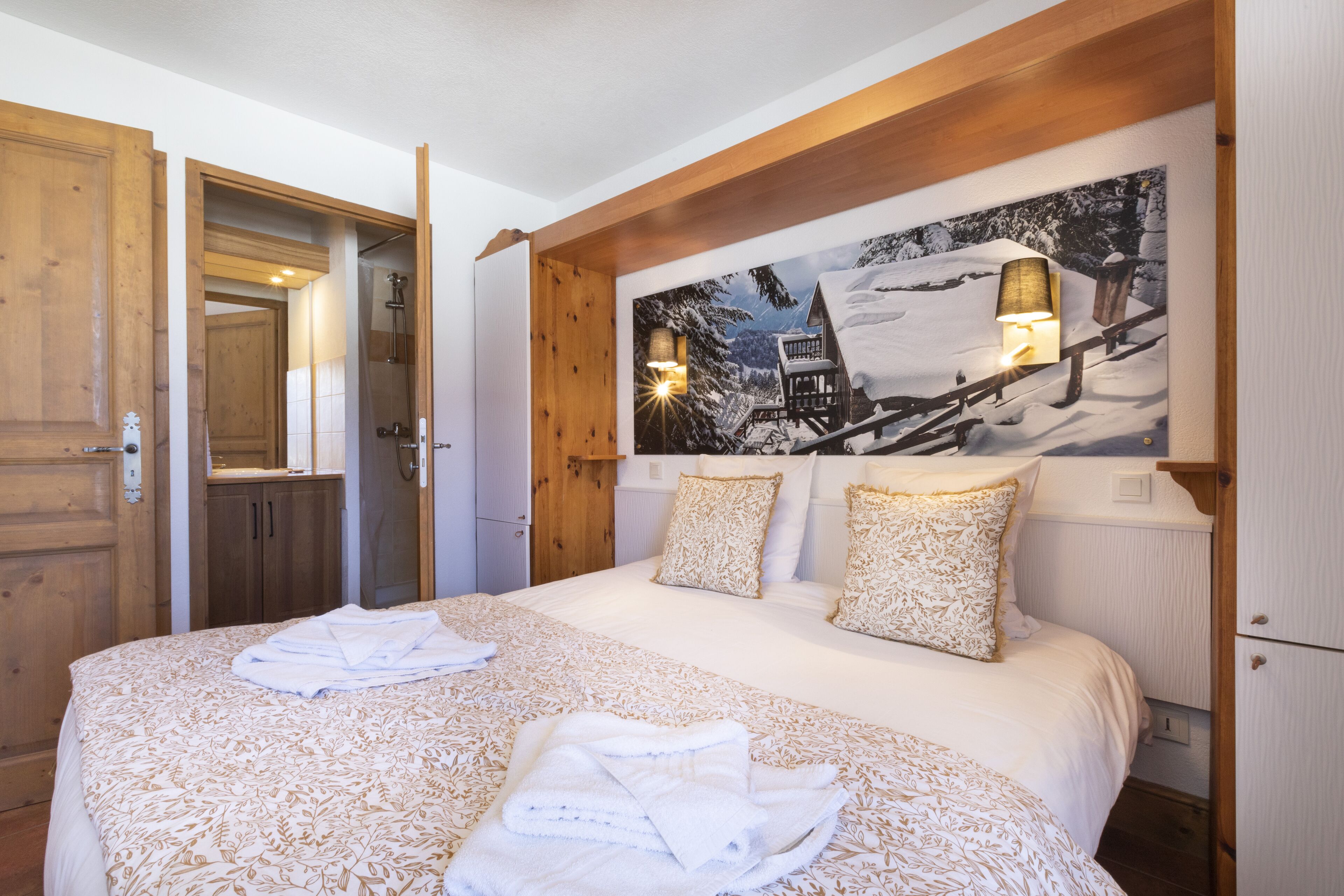 A hotel room with a large bed, wooden headboard, and a winter-themed wall mural.