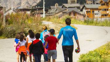 A group of people walking on a paved path with a mountainous backdrop and traditional buildings.